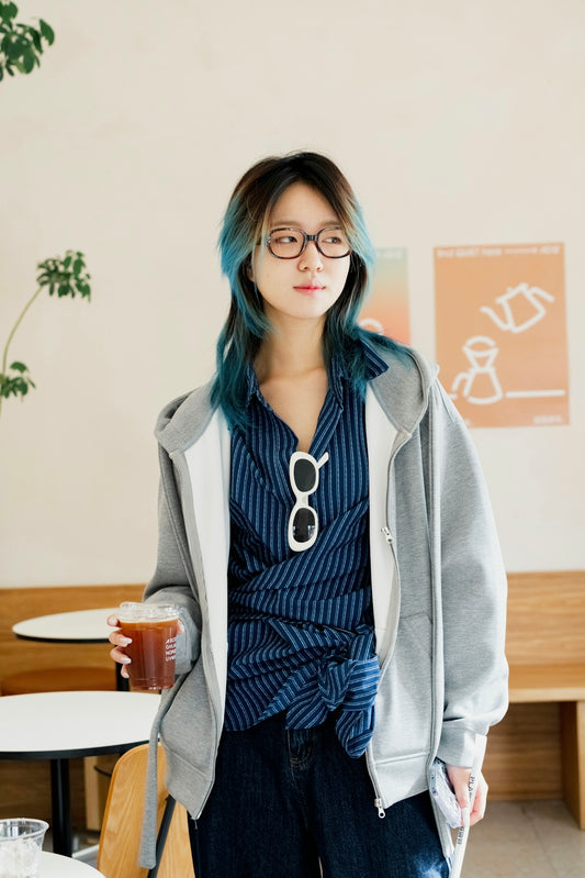 A woman with blue hair and glasses holding a drink